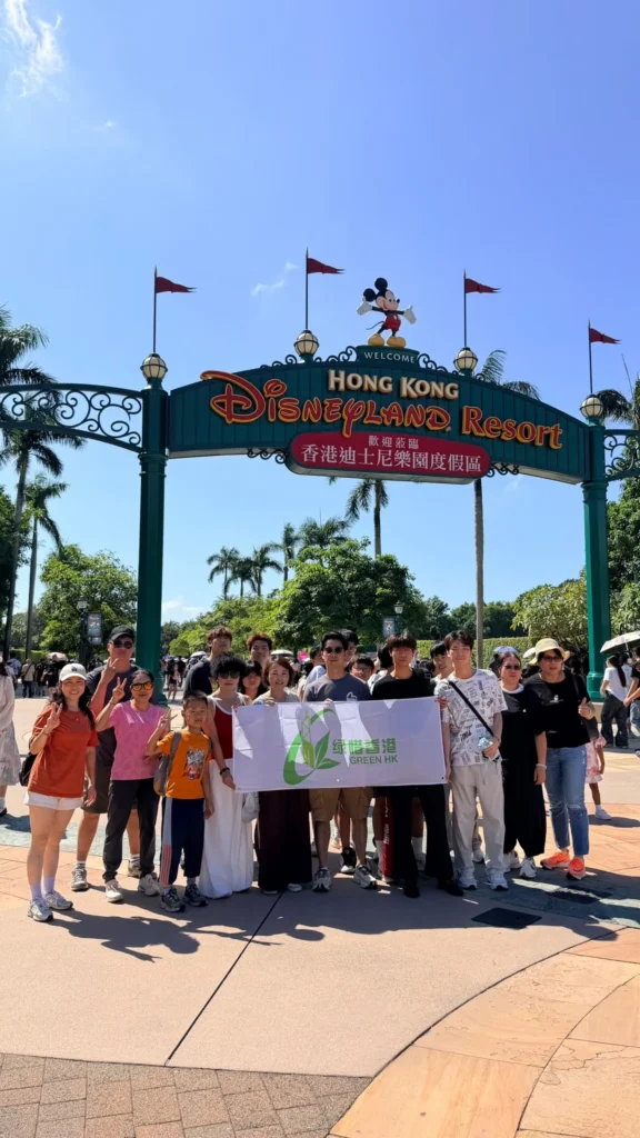 綠惜香港暢遊迪士尼2026，參加者在香港迪士尼樂園入口手持綠惜香港旗幟合照